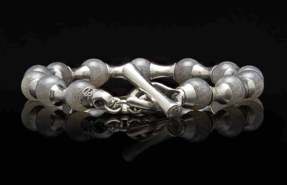 Silver bracelet with rounded, cloudy grey beads and an etched toggle clasp, reflected on a black surface.