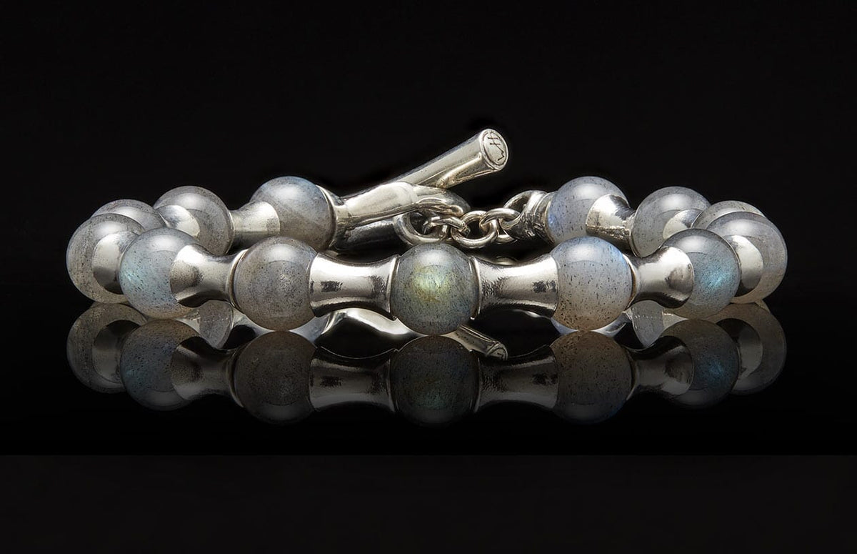 Silver and labradorite beaded bracelet with a toggle clasp on a reflective black surface.