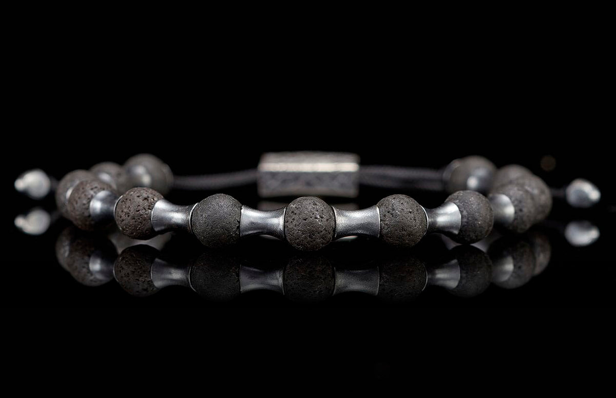 Dark lava stone and silver metal beaded bracelet featuring porous beads and reflective spacers on a black surface.