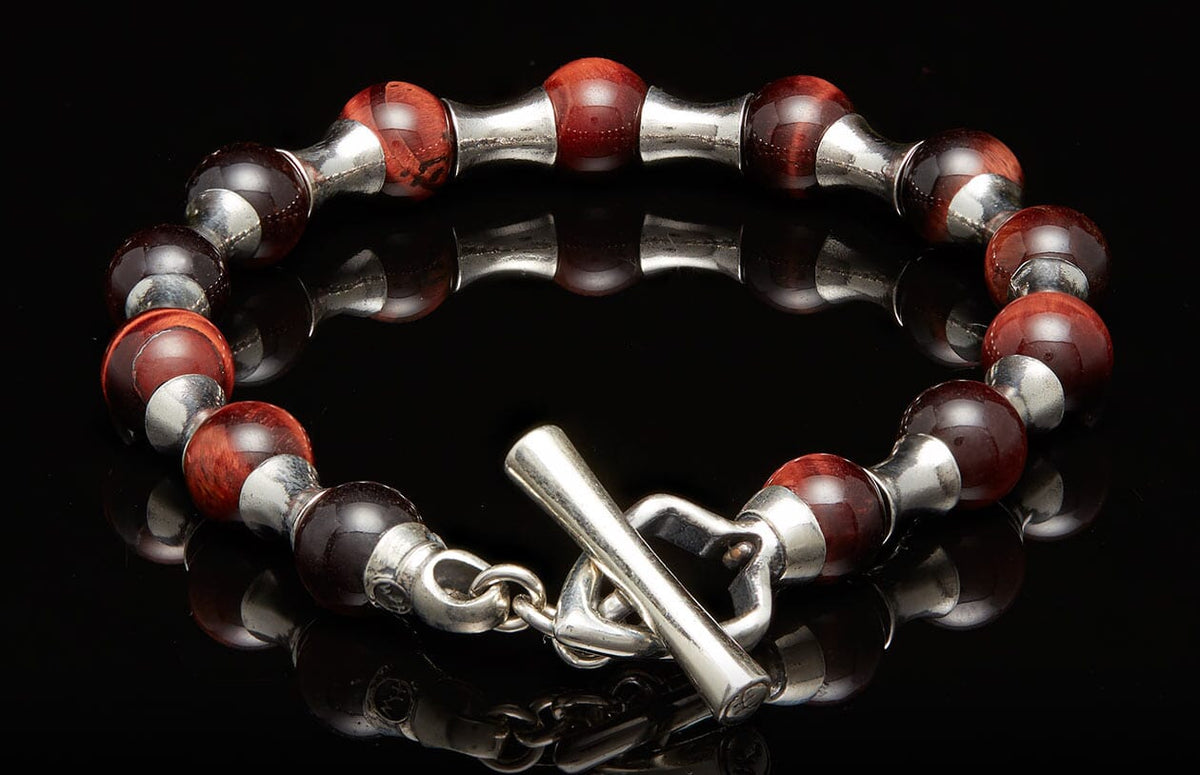Red tiger's eye beaded bracelet with silver spacers and a toggle clasp on a black reflective surface.