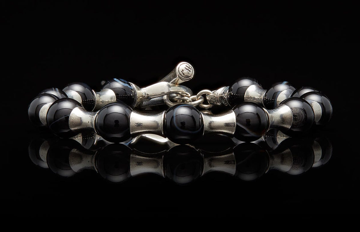 Black agate bead and silver spacer bracelet with a distinctive toggle clasp, reflecting on a dark surface.