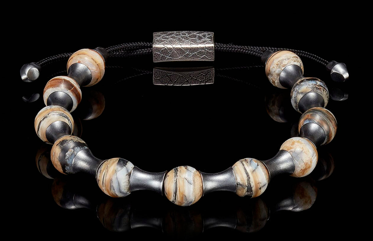 Adjustable bracelet with spherical, naturally banded beads in cream, brown, and black, dark metal spacers, and a hammered clasp.