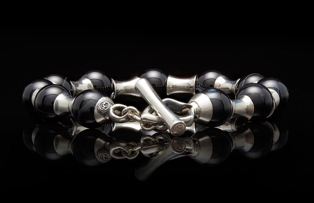 Black and silver beaded bracelet with a toggle clasp featuring engraved symbols, reflected on a dark surface.