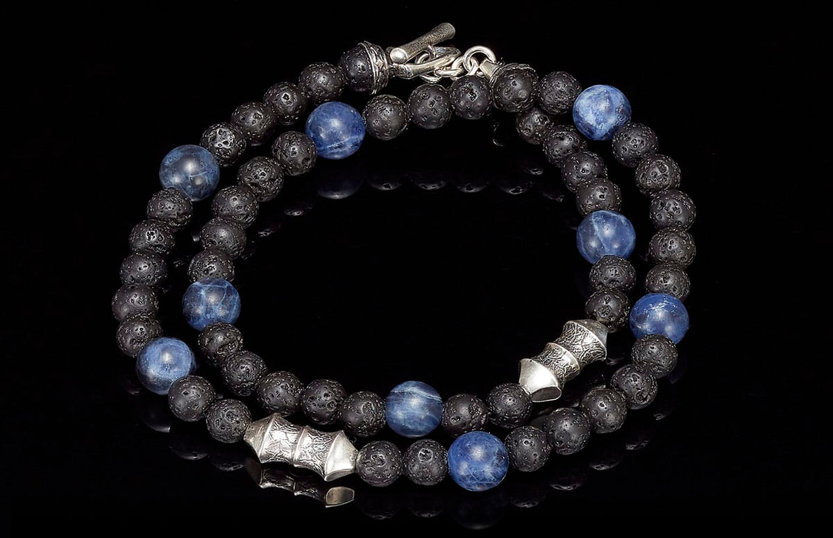 A coiled beaded necklace/bracelet with blue sodalite and black lava beads, featuring ornate silver spacers and clasp.