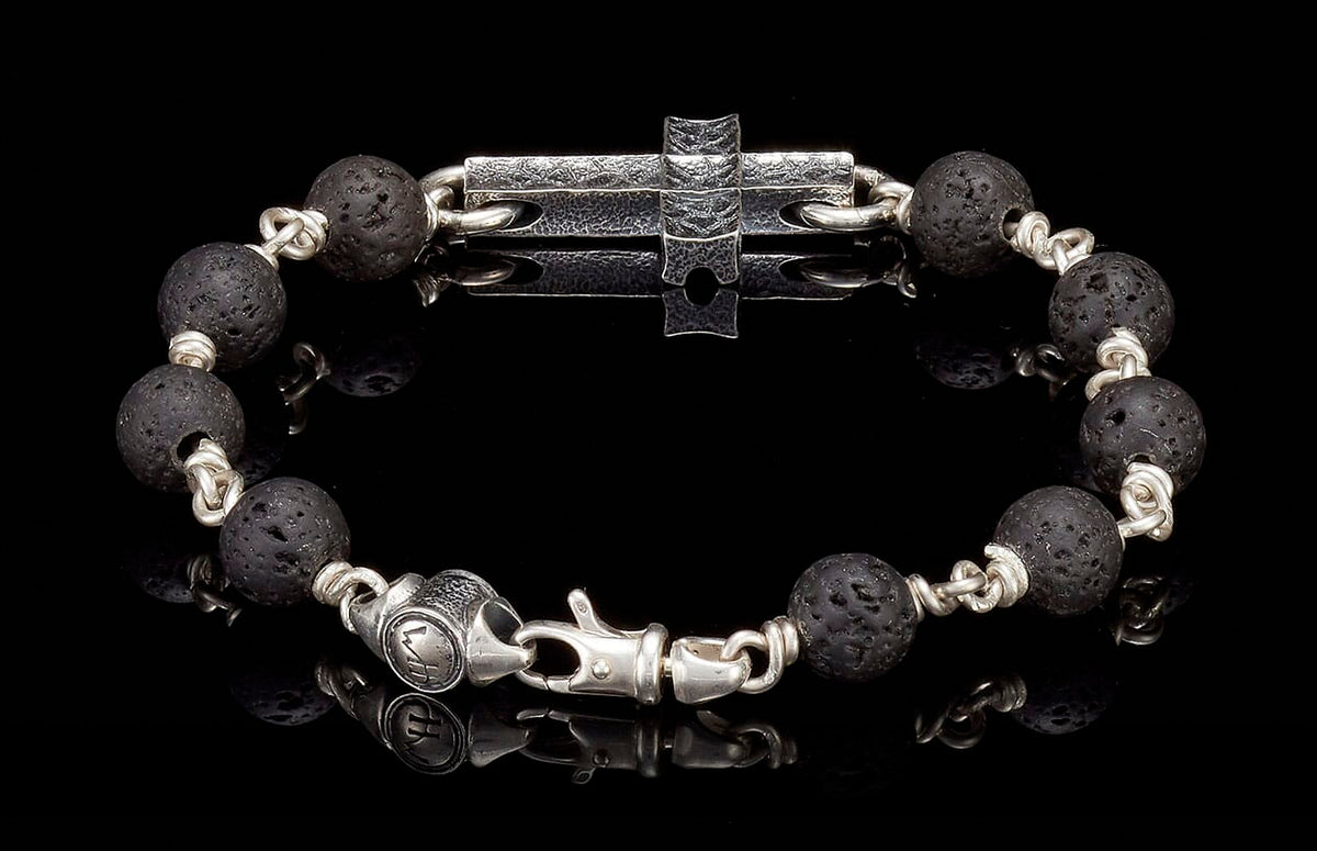 Black lava bead bracelet with silver links, a central hammered silver cross, and an engraved clasp.