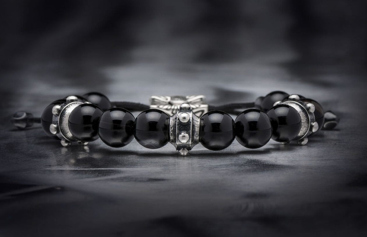 Black sardonyx beaded bracelet with intricate silver metal spacers, lying on a dark textured surface.