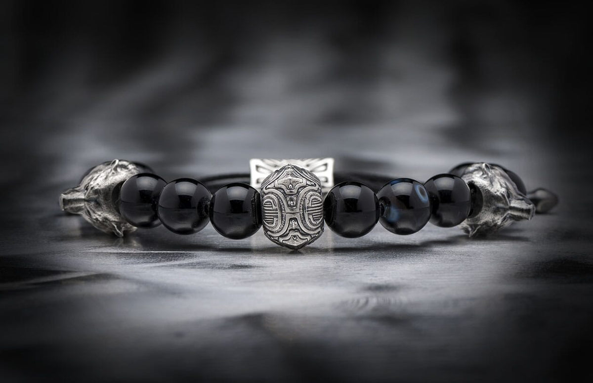Black beaded bracelet with a central intricately patterned silver bead and silver wolf head terminals.