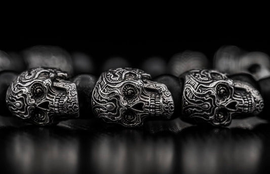 Ornate silver-toned skull jewelry beads with intricate swirling patterns and dark matte beads, in a close-up view.