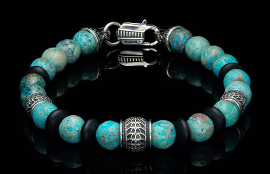 Blue agate and matte black beaded bracelet with ornate silver clasp and patterned silver accent beads on a reflective black surface.
