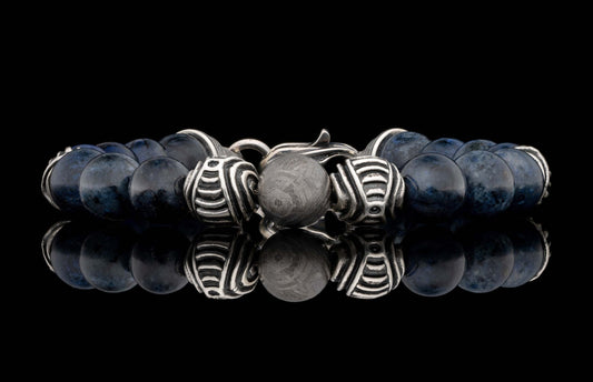 Dark blue beaded bracelet with silver clasp, patterned bead, and textured meteorite bead, reflected.