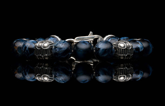 Dark blue beaded bracelet with swirled patterns and ornate silver-colored metal beads, featuring a lobster clasp and reflection on black.