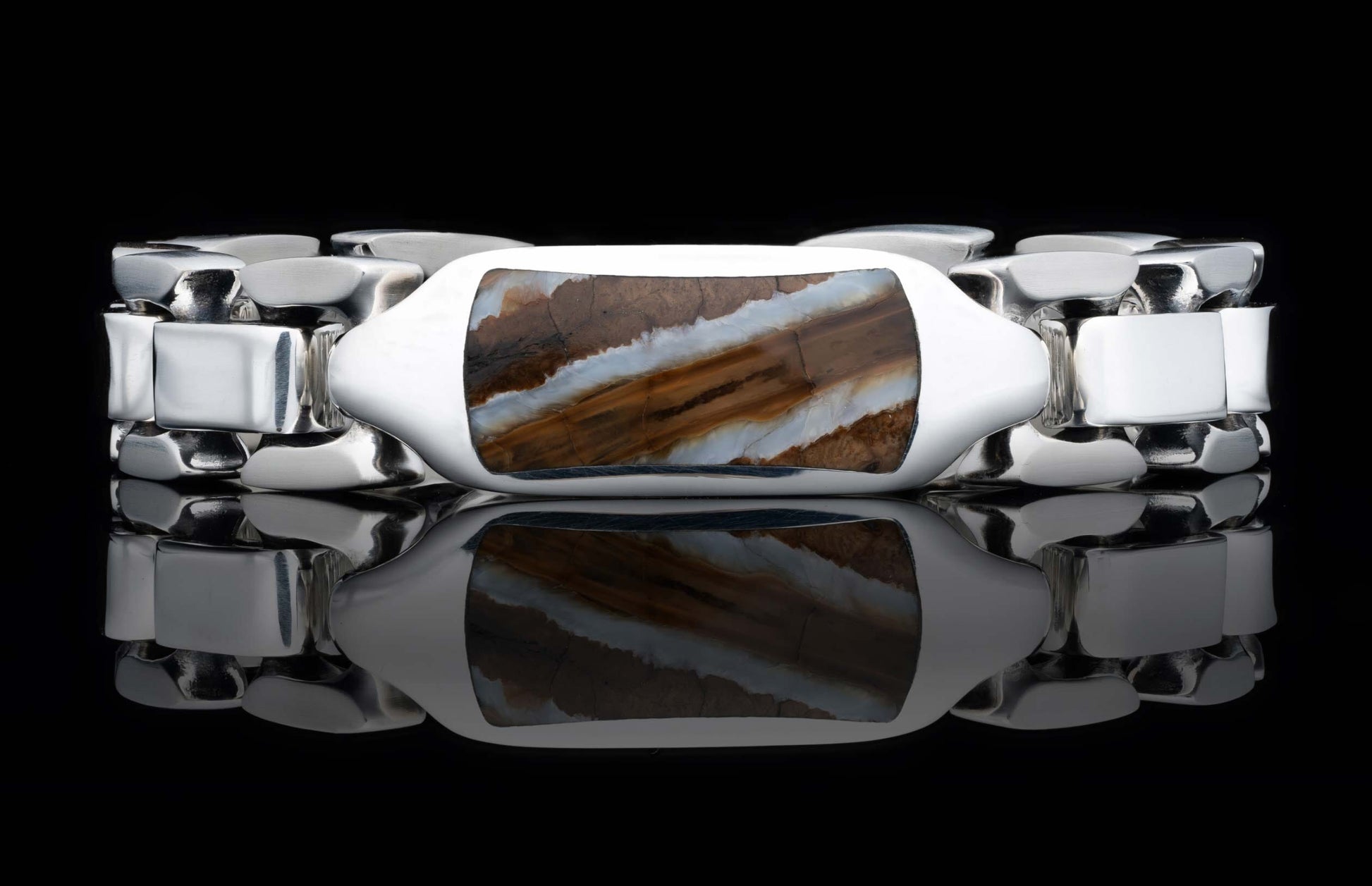 A polished silver link bracelet with a prominent rectangular brown and white striped stone inlay, shown on a reflective black surface.