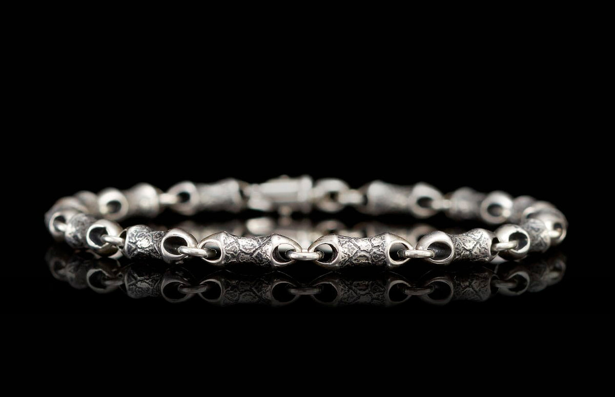 Silver chain bracelet with textured, irregular links and a visible clasp on a reflective black surface.