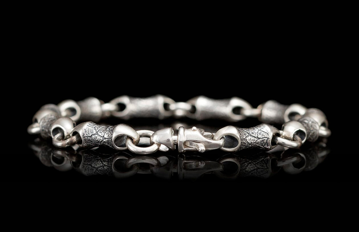 Silver-toned metal bracelet featuring alternating smooth and textured link segments with a distinctive clasp.