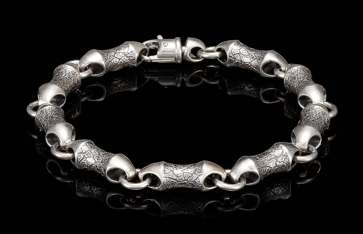 Silver-toned metal bracelet with textured cylindrical links, smooth connecting rings, and a prominent box clasp.