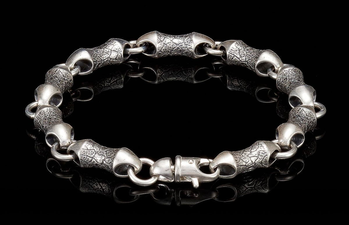 Silver bracelet with textured, scale-like links and a lobster clasp on a reflective black surface.