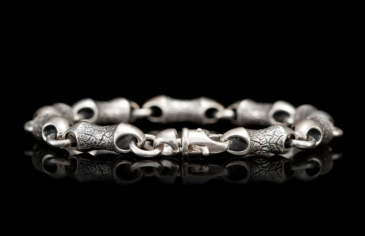 Textured silver bracelet with distinct links and a lobster clasp, reflecting on black.