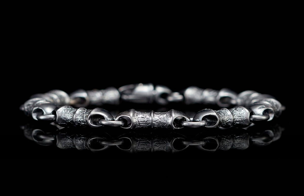 Textured dark silver-toned linked bracelet reflecting on a glossy black surface.