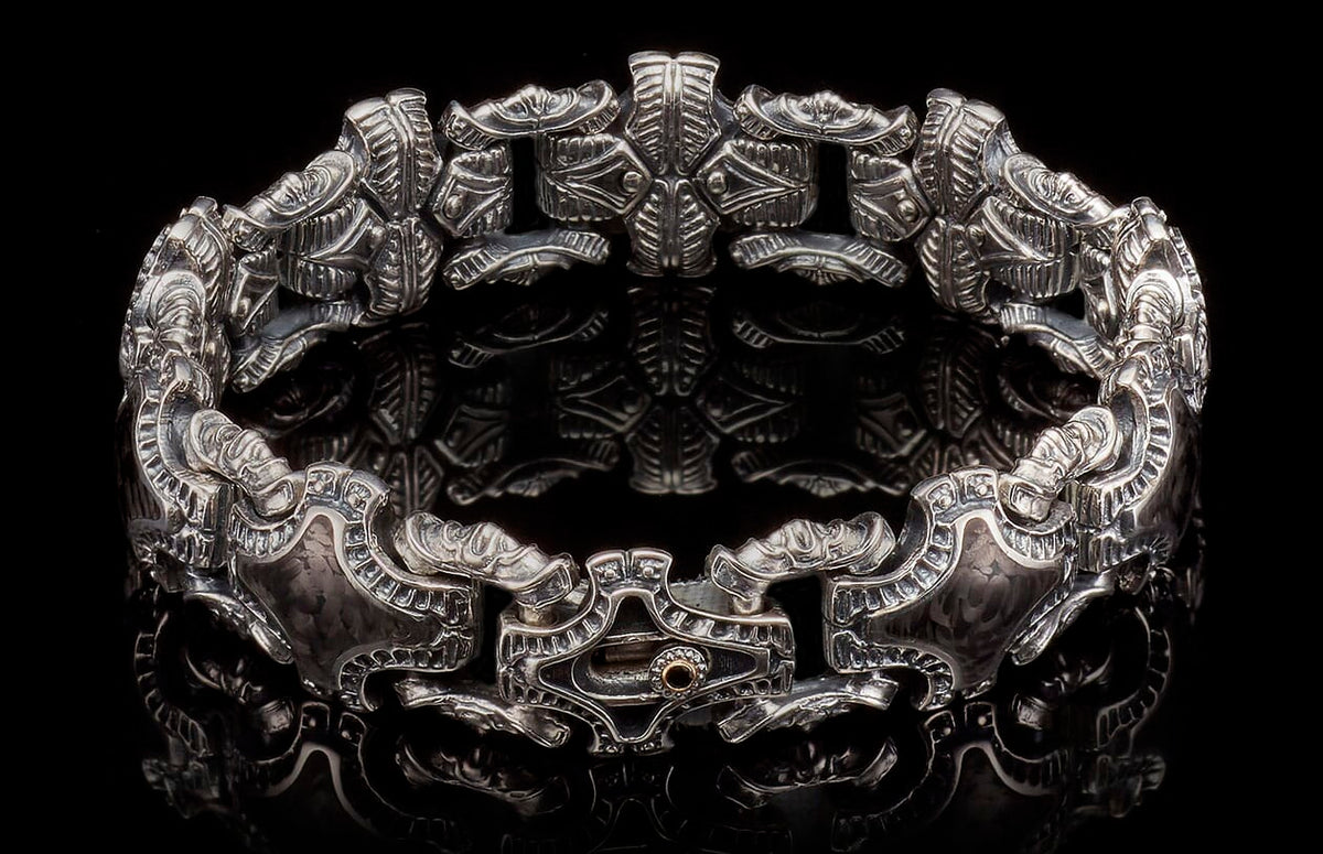 Ornate silver cuff bracelet with intricate carved patterns and a copper-toned accent on the clasp, reflecting on black.