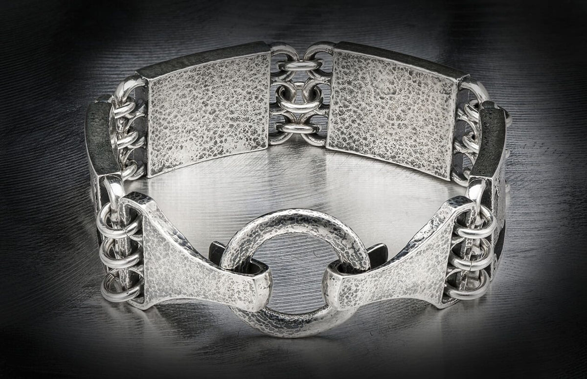 Textured silver-toned metal bracelet with wide hammered links, connected by smooth rings, and a central textured hoop.