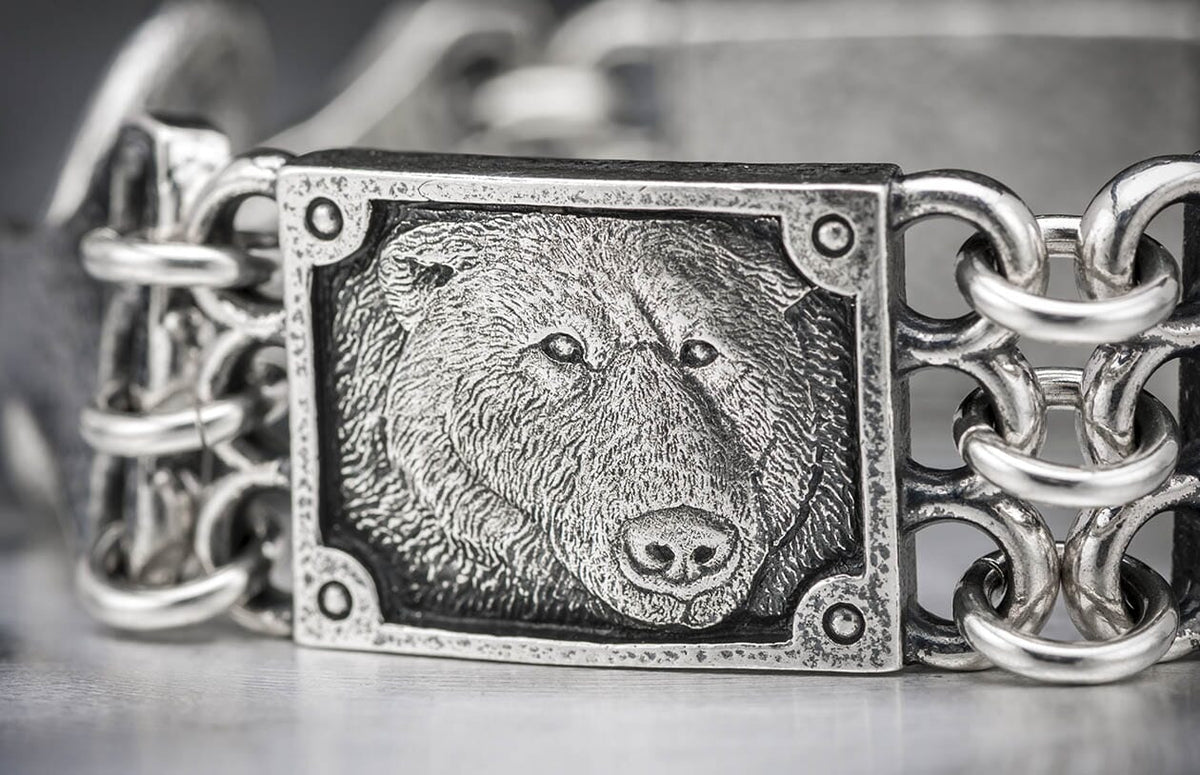 Close-up of a silver bracelet featuring a textured bear head panel and interlocking chain links.