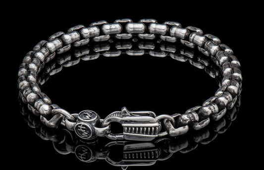 Silver chain bracelet with hammered, textured links and an ornate clasp, on a black reflective surface.