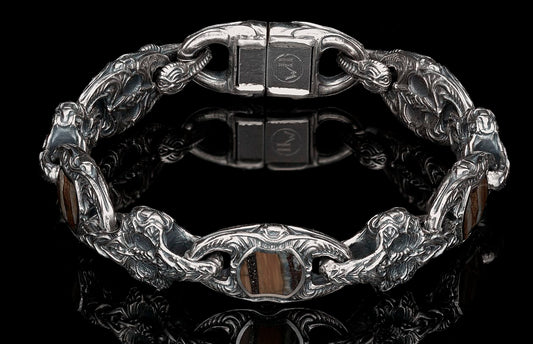 Silver bracelet with ornate dragon-head links and brown striped stone inserts, displayed on a reflective black surface.