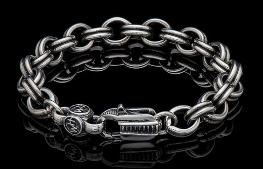 Silver chain link bracelet with chunky oval links and a decorative clasp on a reflective black surface.