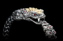Ornate silver and gold snake-head bracelet with ruby eyes, fangs, and a braided black and silver band.