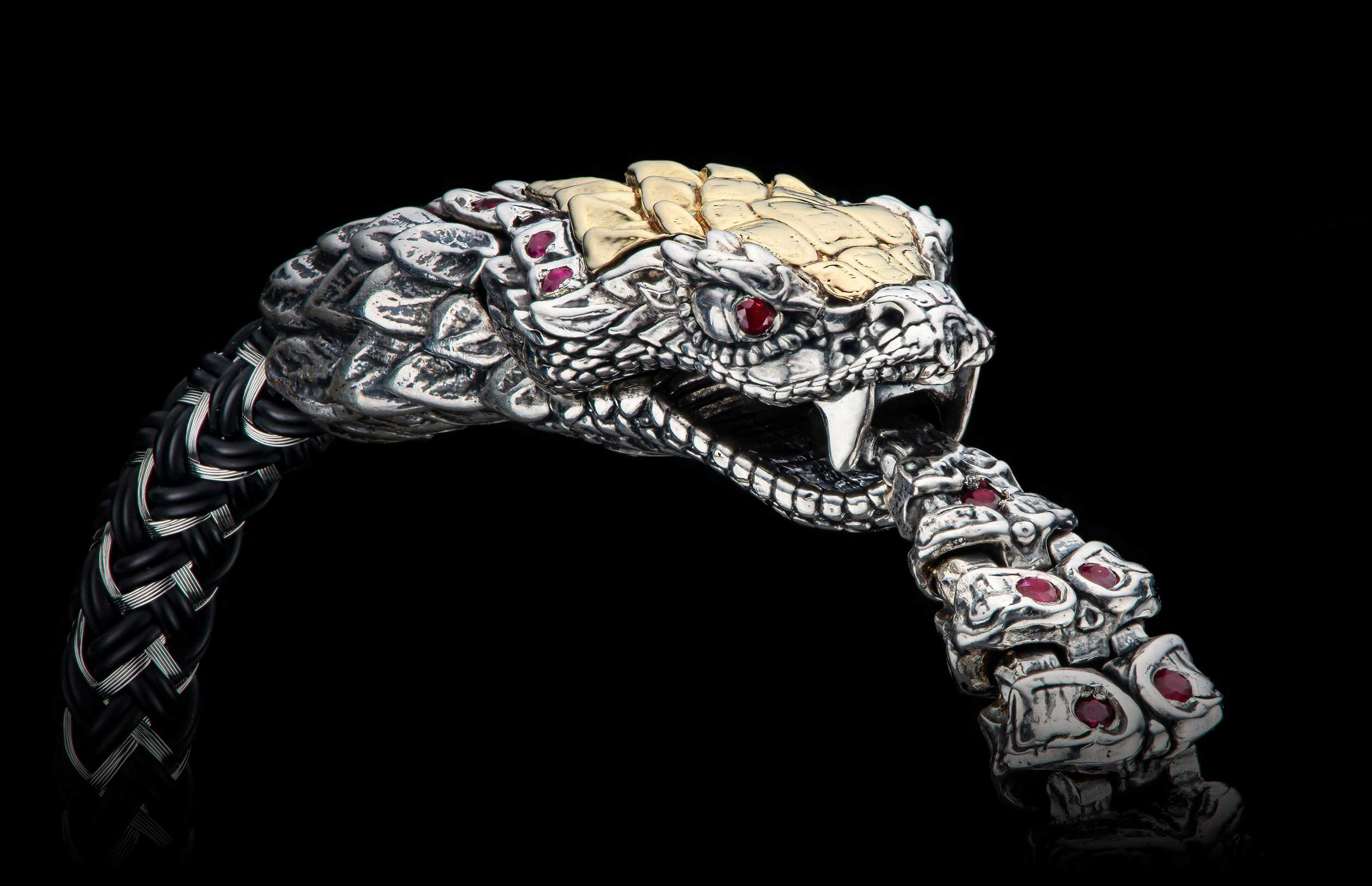 Ornate silver and gold snake-head bracelet with ruby eyes, fangs, and a braided black and silver band.