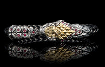 Silver and gold snake-design bracelet with red gemstones and intricate scale textures, on a black reflective surface.