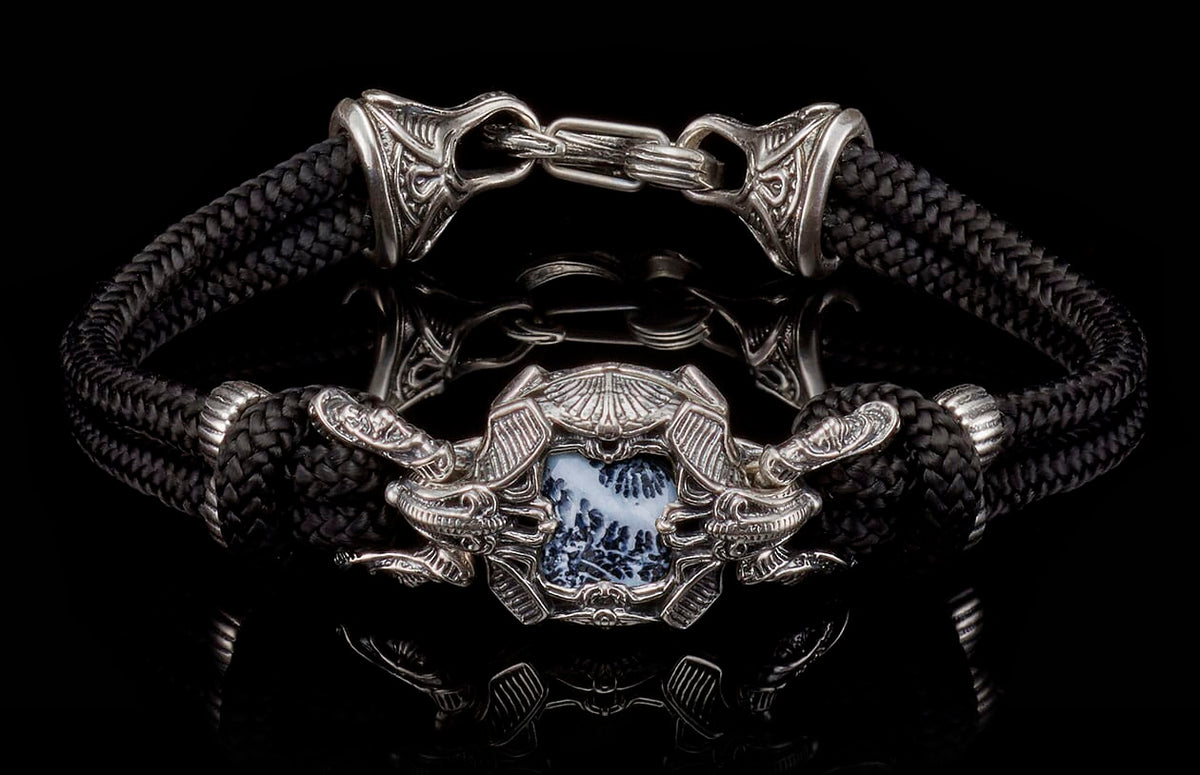 Black braided cord and silver bracelet with an ornate central medallion, white and black patterned stone, flanked by dragon heads, and intricate clasp.