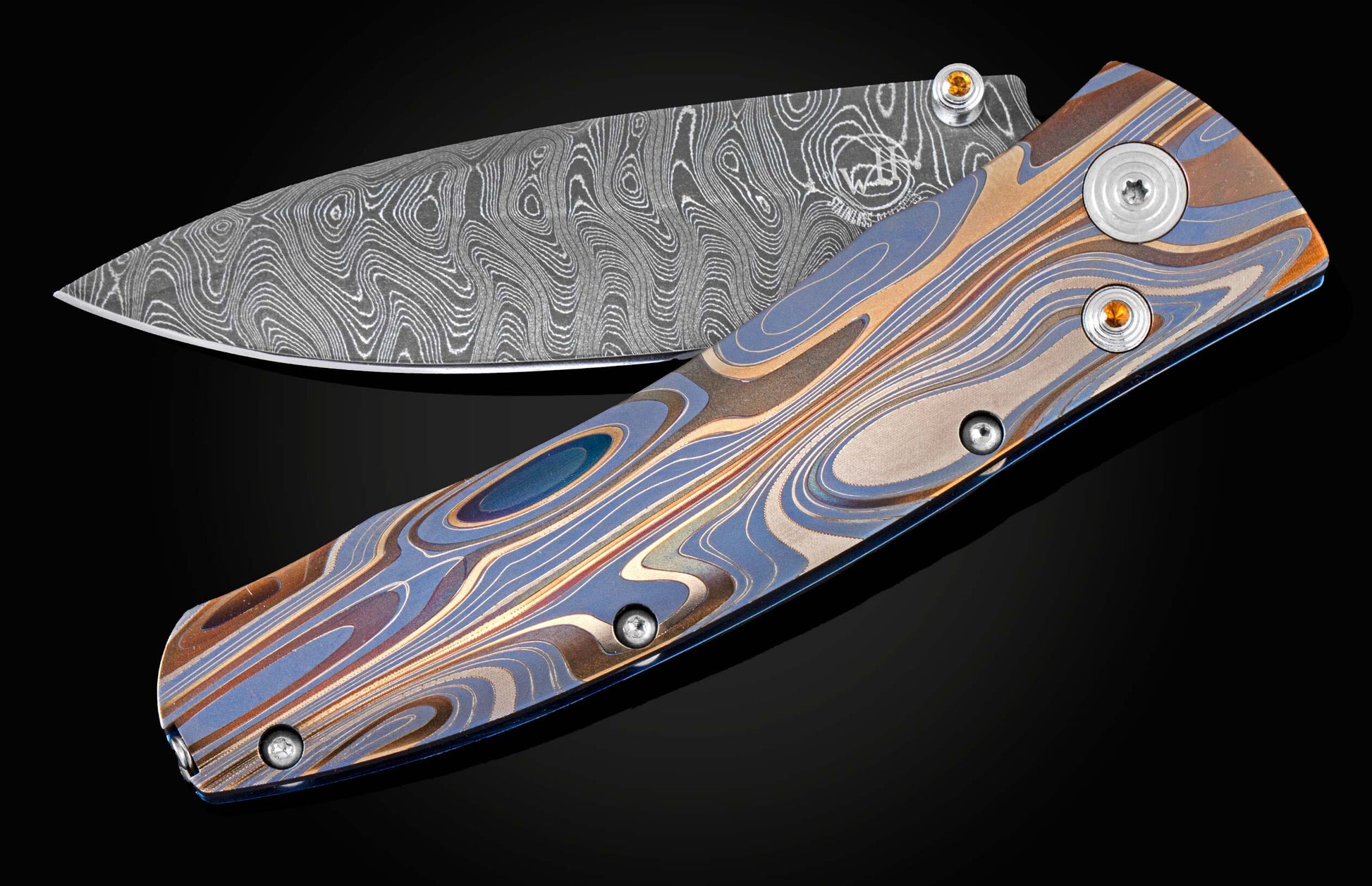 Handcrafted pocketknife from William Henry features a light and resilient titanium frame that is laser-engraved in swirls of color. The blade is hand-forged damascus steel. The button lock and thumb stud are inset with citrine gemstones.