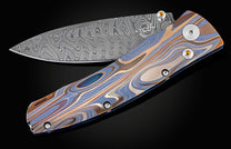 Handcrafted pocketknife from William Henry features a light and resilient titanium frame that is laser-engraved in swirls of color. The blade is hand-forged damascus steel. The button lock and thumb stud are inset with citrine gemstones.