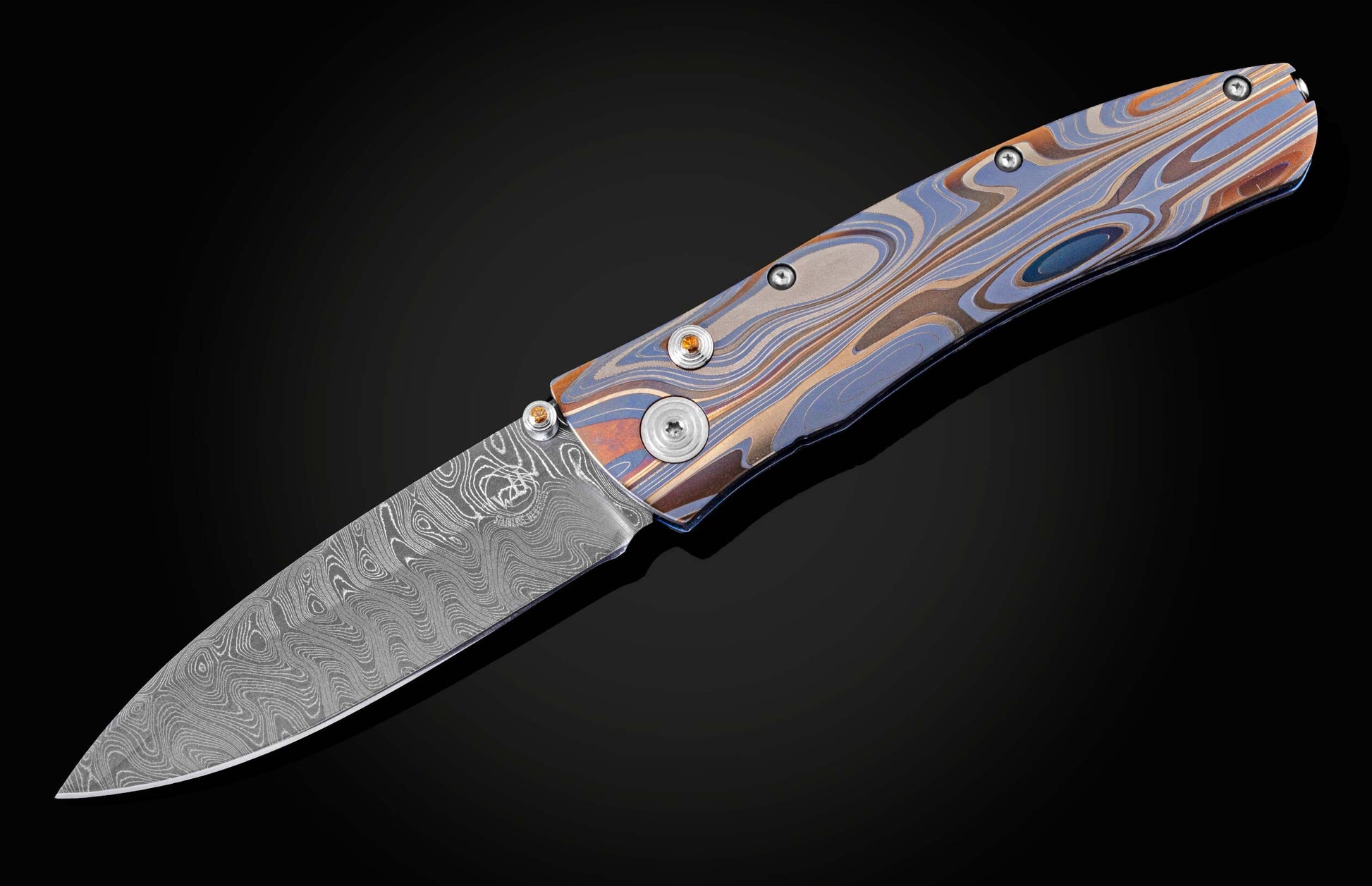 Handcrafted pocketknife from William Henry features a light and resilient titanium frame that is laser-engraved in swirls of color. The blade is hand-forged damascus steel. The button lock and thumb stud are inset with citrine gemstones.