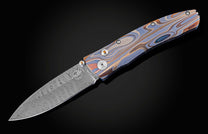 Handcrafted pocketknife from William Henry features a light and resilient titanium frame that is laser-engraved in swirls of color. The blade is hand-forged damascus steel. The button lock and thumb stud are inset with citrine gemstones.