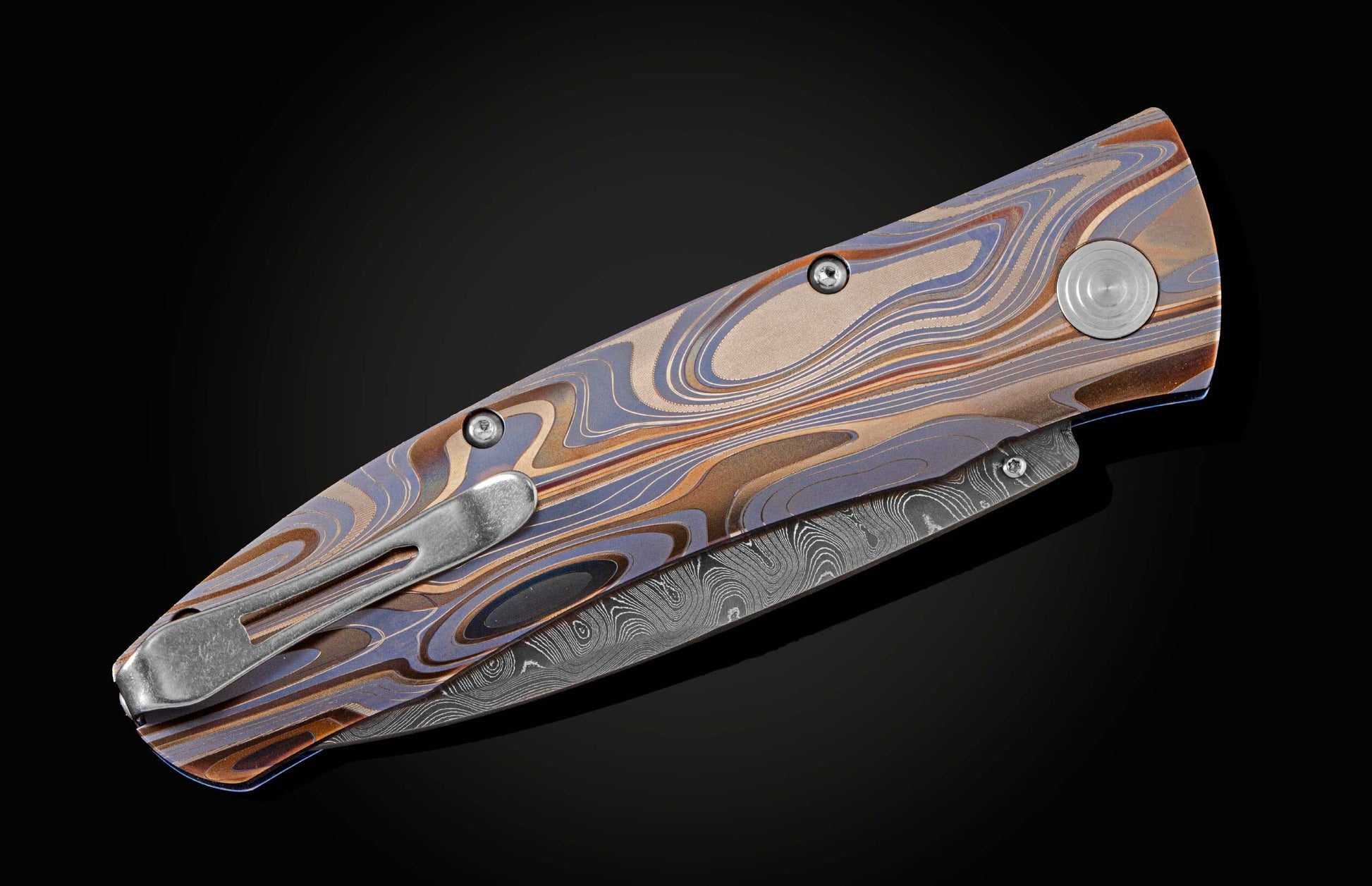 Handcrafted pocketknife from William Henry features a light and resilient titanium frame that is laser-engraved in swirls of color. The blade is hand-forged damascus steel. The button lock and thumb stud are inset with citrine gemstones.