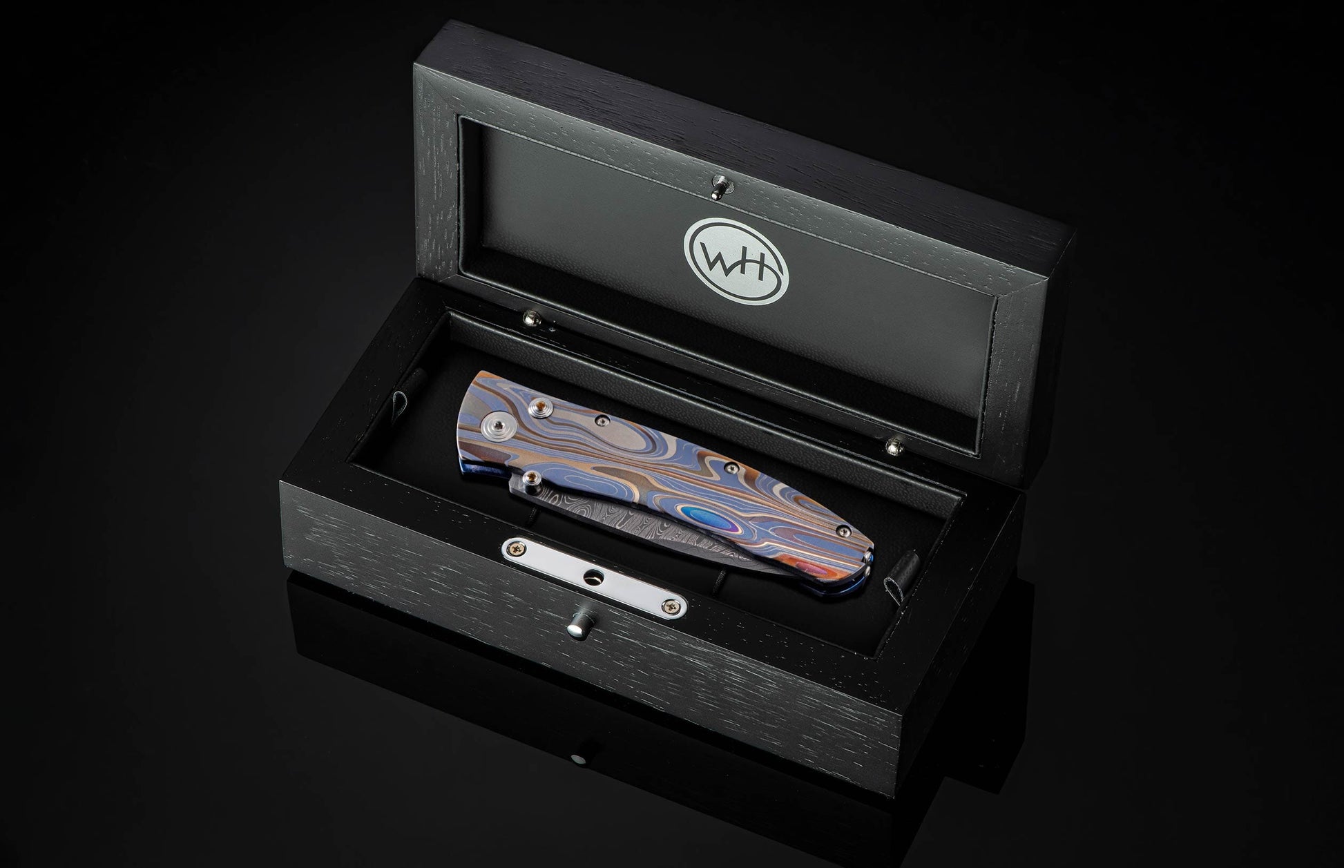Handcrafted pocketknife from William Henry features a light and resilient titanium frame that is laser-engraved in swirls of color. The blade is hand-forged damascus steel. The button lock and thumb stud are inset with citrine gemstones.
