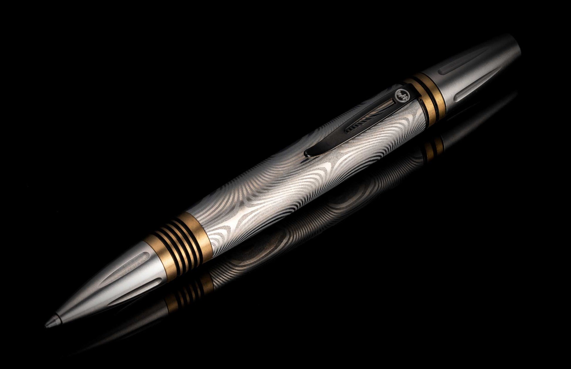 A classic executive pen from William Henry. The distinctive Damascus steel barrel is flanked by brass spacers with deep grooves, and the tip and top section are crafted from stainless steel with art deco details. The pen is displayed on a black background
