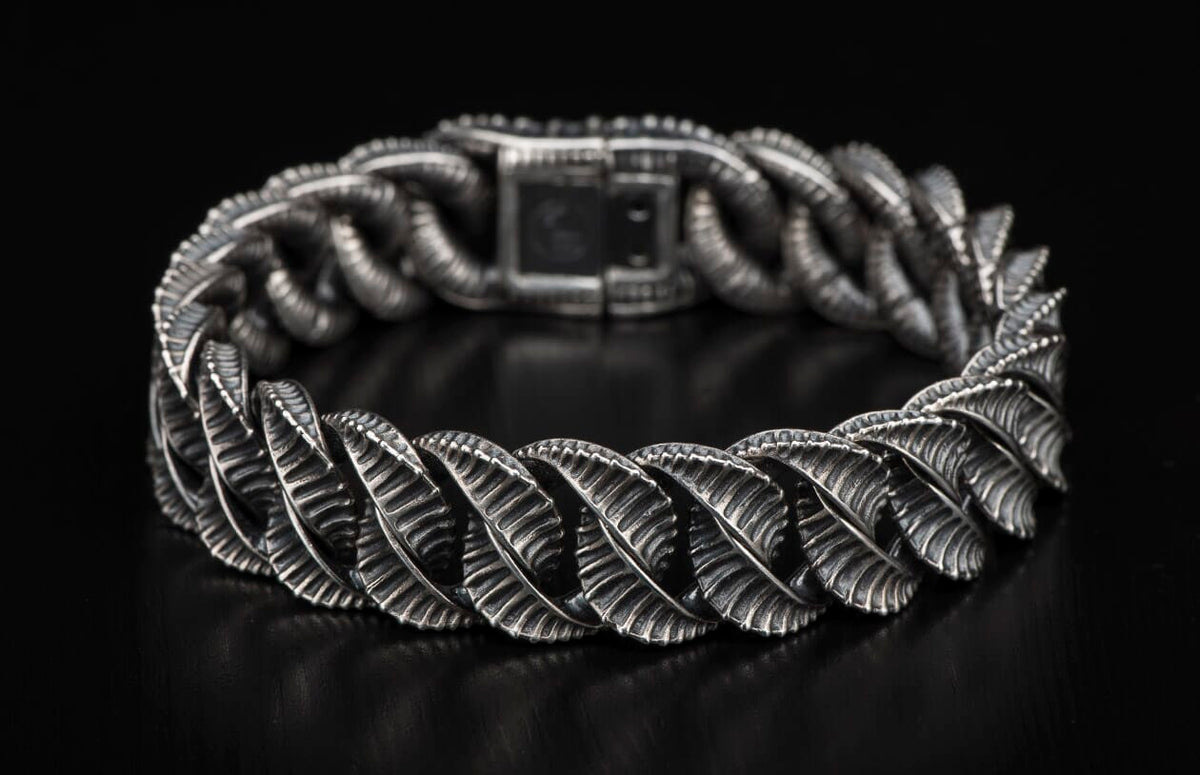 Silver bracelet with intricate leaf-like textured links laid on a dark surface.