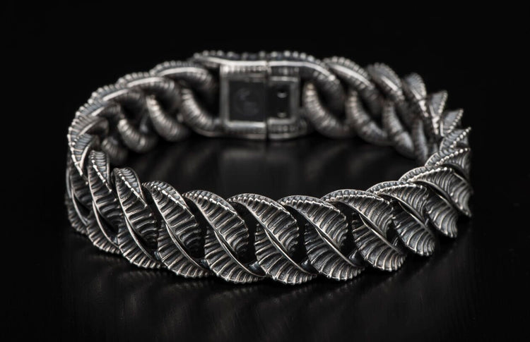 Silver bracelet with intricate leaf-like textured links laid on a dark surface.