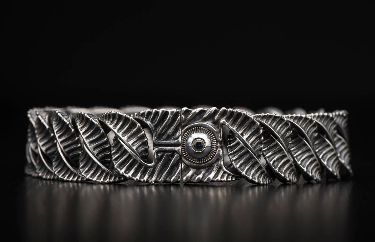Oxidized silver bracelet with intricate leaf-like links and a central ribbed clasp featuring a dark gem.