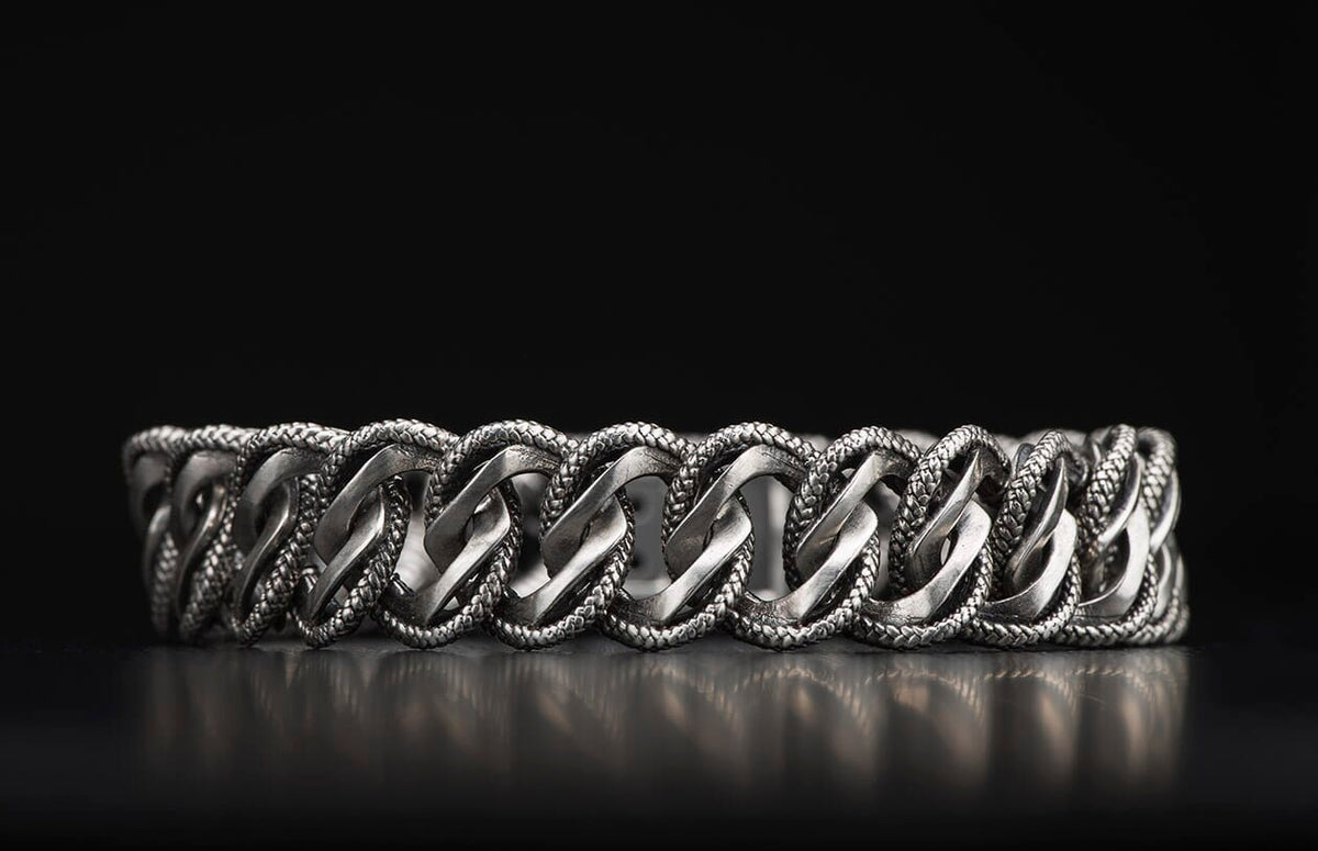 Silver-toned Pasha bracelet with interlocking smooth and braided chain links, reflecting on a dark surface.