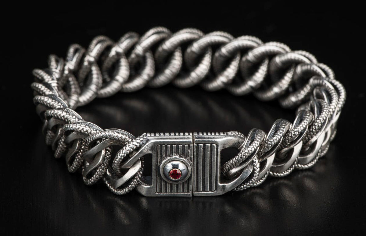 Silver-tone chunky chain bracelet with braided textured links and a decorative clasp featuring a red gemstone.
