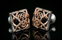 Square silver cufflinks with a rose gold cage-like skull design over a black background, showing reflections.