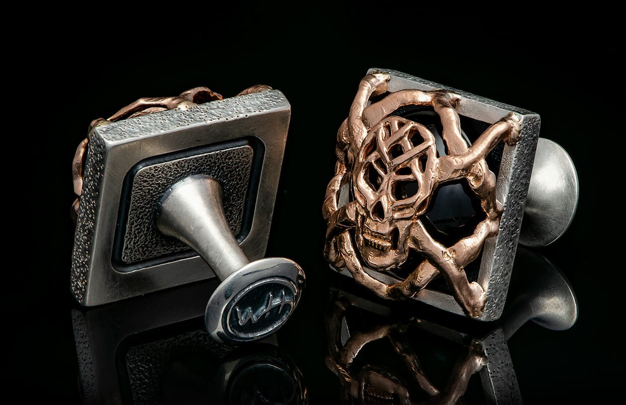 Silver and bronze-toned cufflinks with skull design, black stone, and textured square frames.