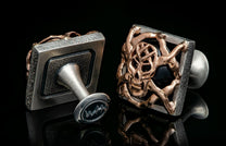 Silver and bronze-toned cufflinks with skull design, black stone, and textured square frames.