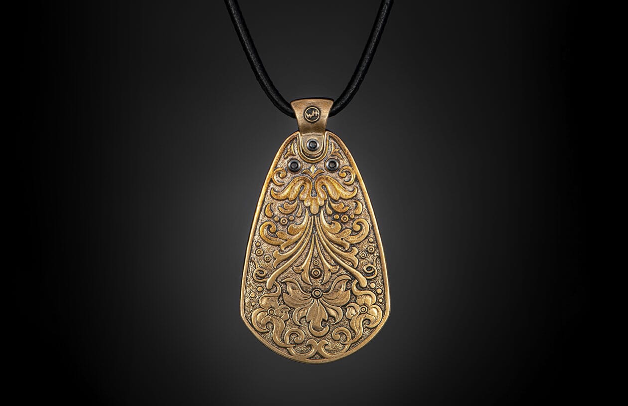 Bronze pendant with ornate floral and scrollwork designs, featuring dark accents, hanging on a black cord.