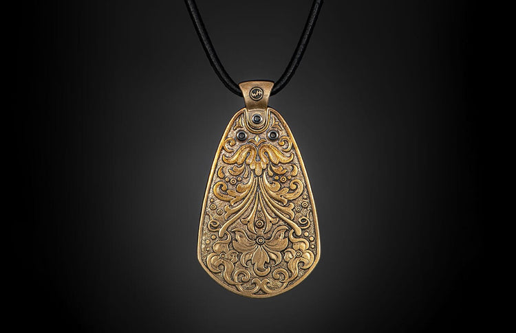 Bronze pendant with ornate floral and scrollwork designs, featuring dark accents, hanging on a black cord.