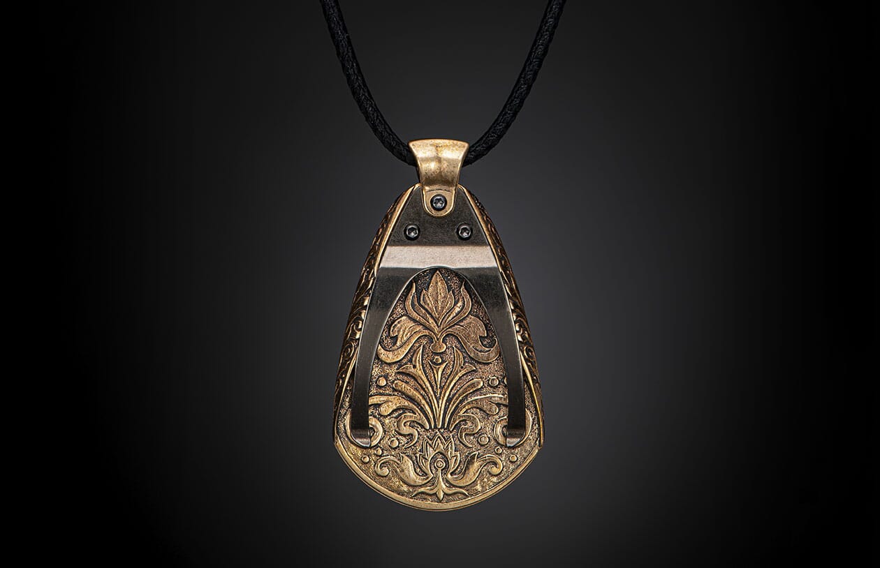 Ornate metallic bronze pendant with intricate floral and scrollwork relief, suspended from a black braided cord.